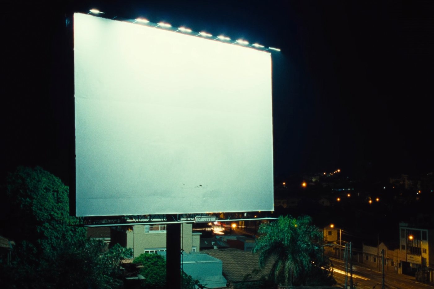 Face de outdoor em branco, iluminada por refletores, sobre uma avenida de cidade brasileira à noite